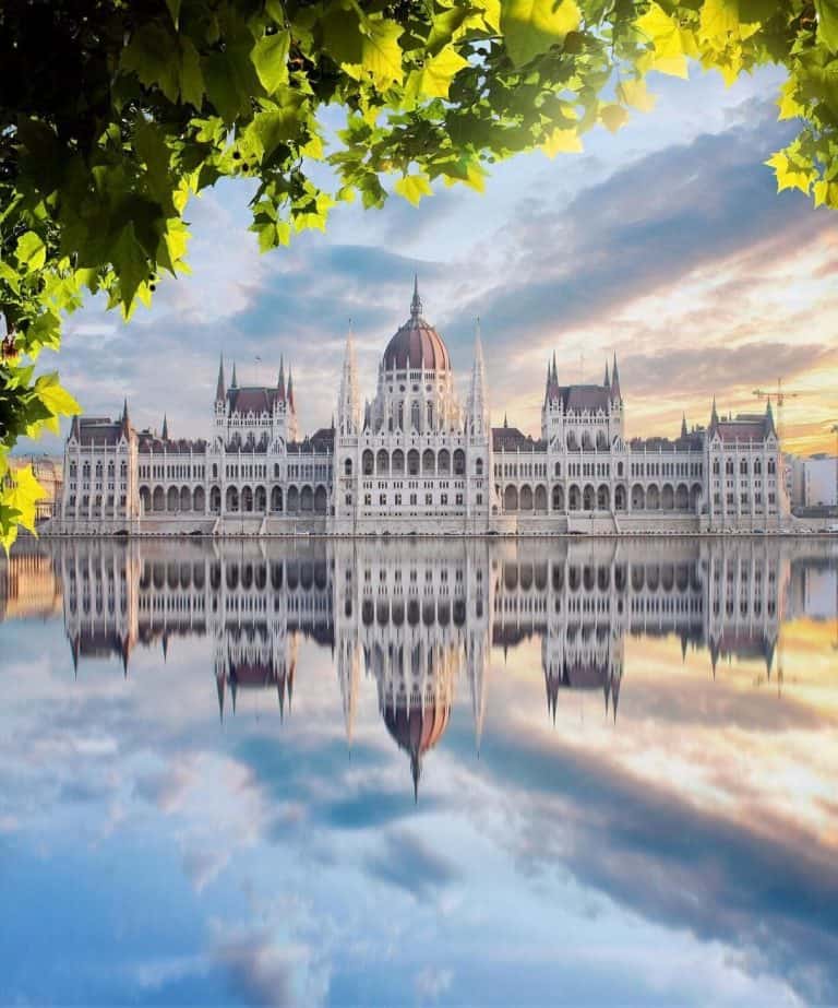Budapest Parliament seen from behind green spring trees across the river.