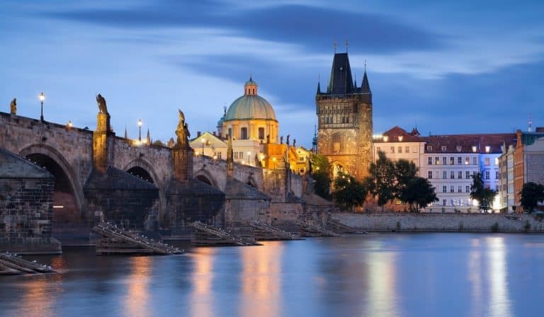10 Off the Beaten Path Things to do in Prague 1 Prague bridge over river at dusk with the lights reflecting on the river.