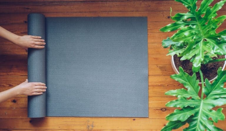 Top 8 Environmentally Friendly Yoga Mats 18 Hands rolling up a yoga mat next to large green, leafy plants.